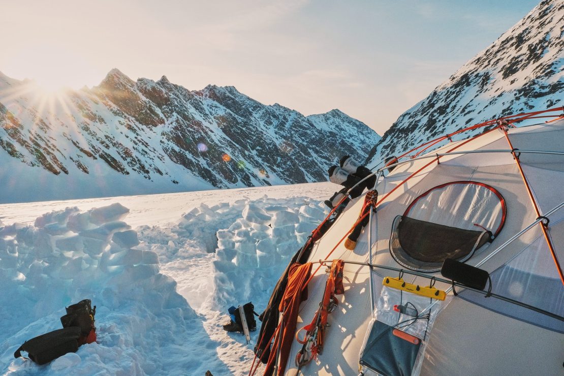 Golden light casting on an expedition dome tent with gear hanging off of it.