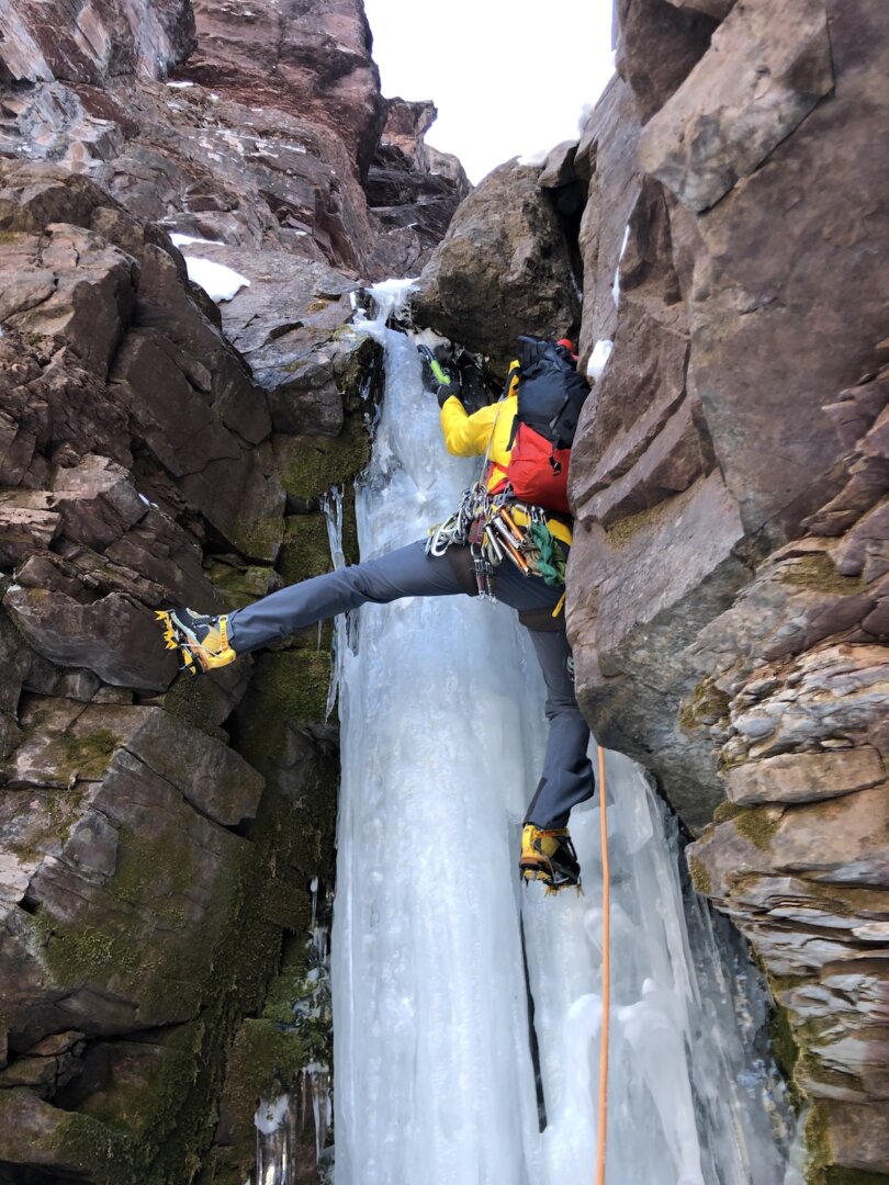 San Juan Expeditions guide climbing an ice pillar with a foot flagged out onto rock.